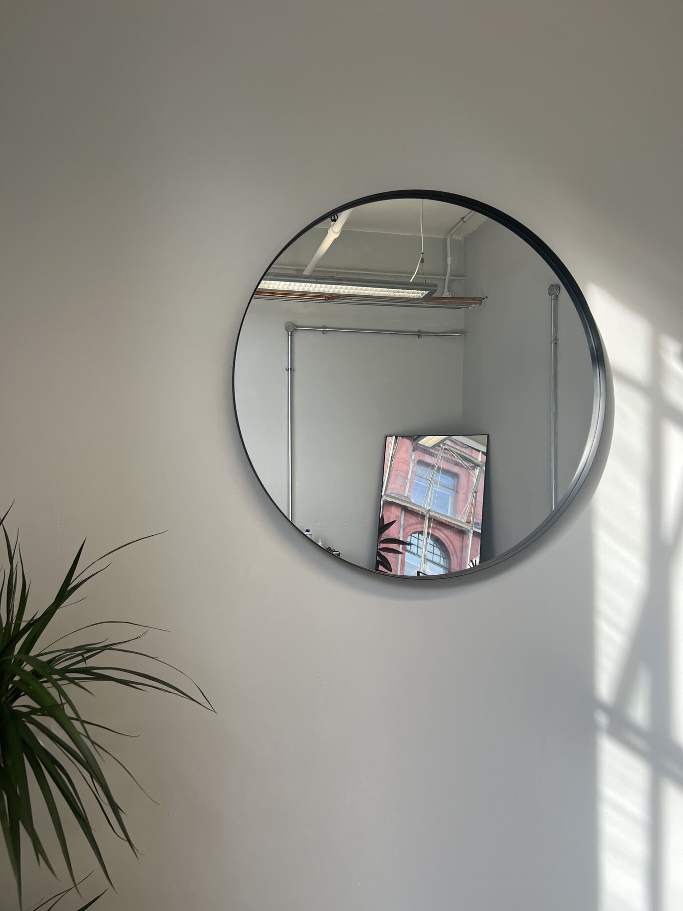 Round black-framed mirror reflecting red Manchester brickwork